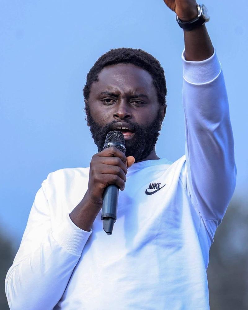 John Methu speaking into a microphone, arm raised
